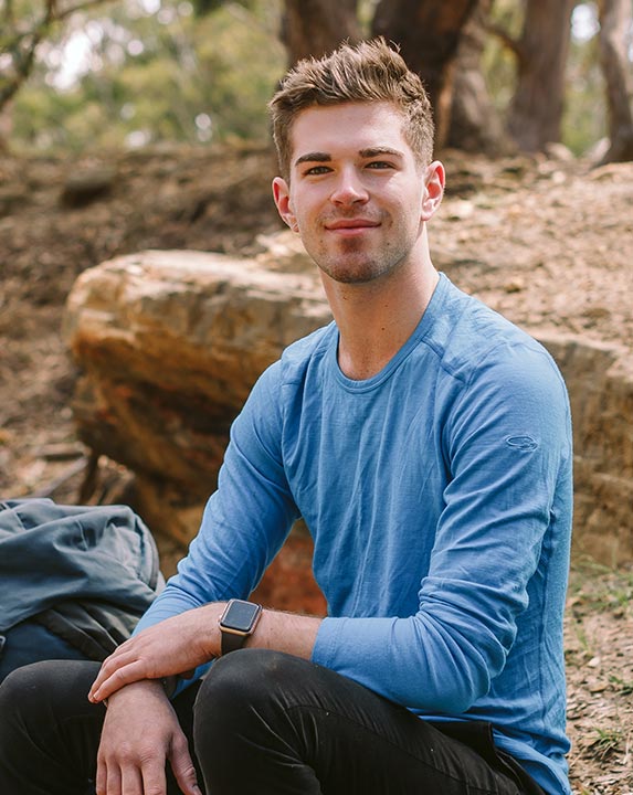 Canteen young person, Daniel, who found community in Canteen after his mum was diagnosed with cancer, sitting in the woods smiling to the camera