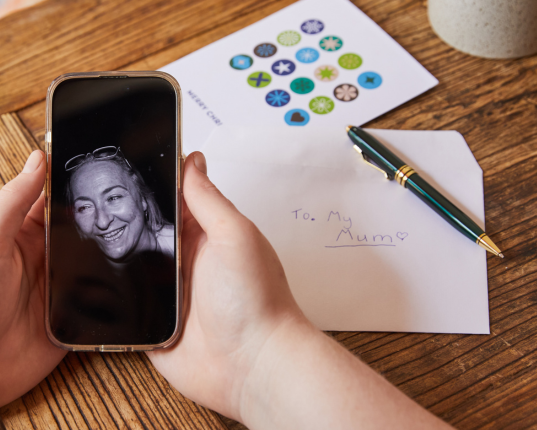 A phone displaying a black and white photo of a Canteen young person's mother alongside a note that reads "to mum". Olivia lost her mum to cancer 