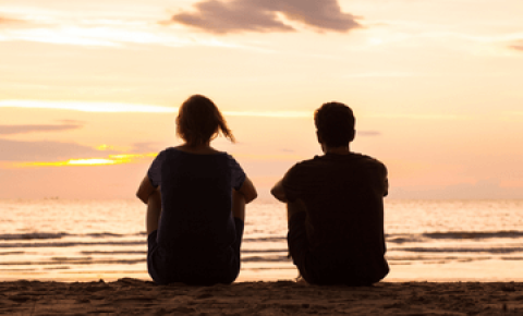 Mum and son sit on beach looking into the sunset