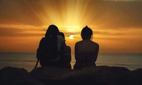 three young people sitting and looking into the sunset