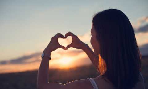 young person making a heart shape with her hands in front of the sky