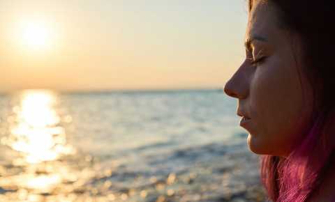 Young woman with eyes closed looking out onto the ocean