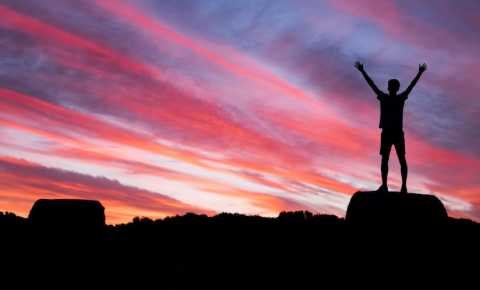 young person standing on a rock with their arms up looking into the sunset. life after cancer image