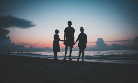 Three siblings hold hands on a beach