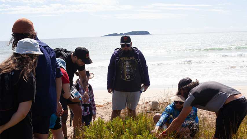 group of young people at the beach looking at plants during the canteen first nations cultural program