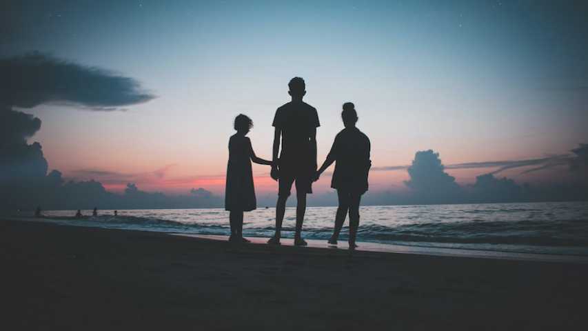 Three siblings hold hands on a beach